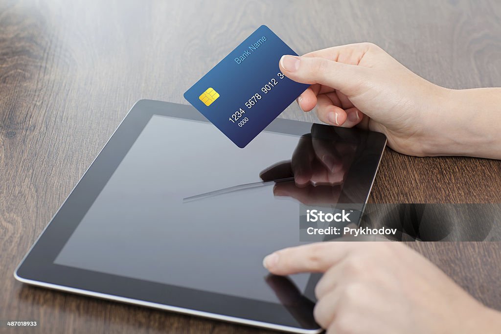 female hands holding credit card and a computer female hands holding credit card and a computer tablet on the table in the office Electronics Store Stock Photo