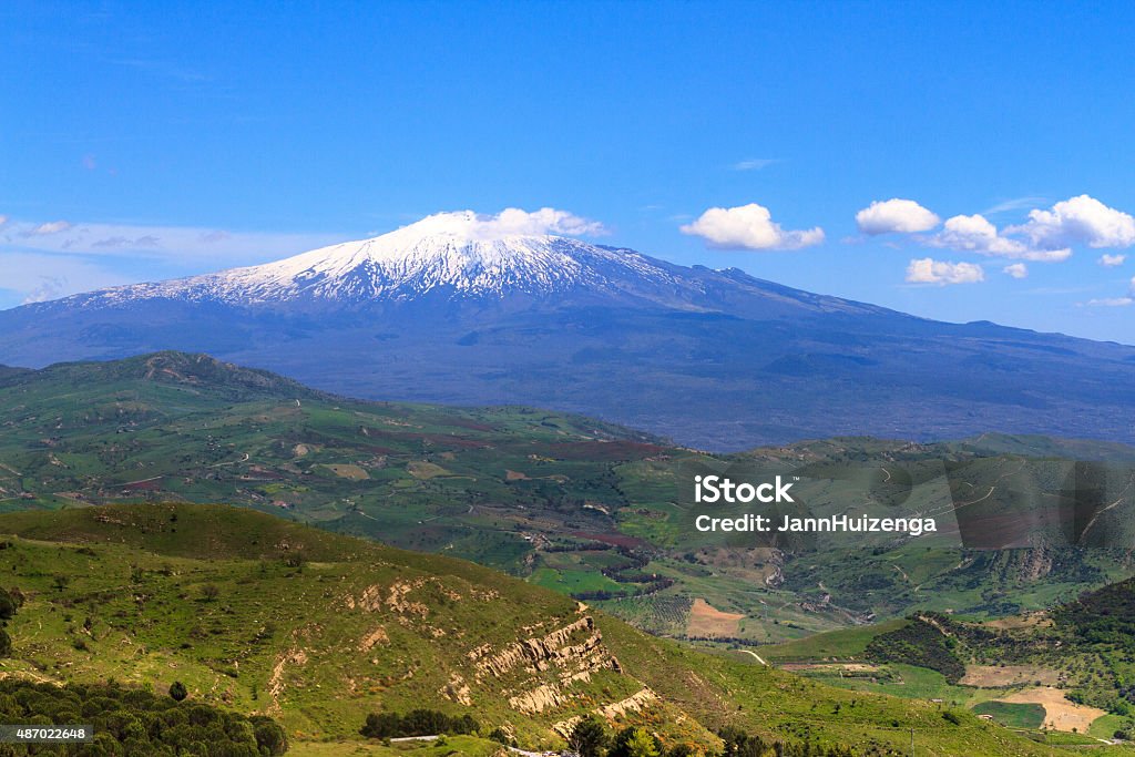 Panorama of Mount Etna in Spring, Sicily A tranquil, bucolic panorama of snowy Mt. Etna in spring, with blue sky and puffy clouds coming from the volcanic cone, and hilly green countryside in front. Shot from Troina (Enna Province). Copy space in the sky. Mt. Etna Stock Photo