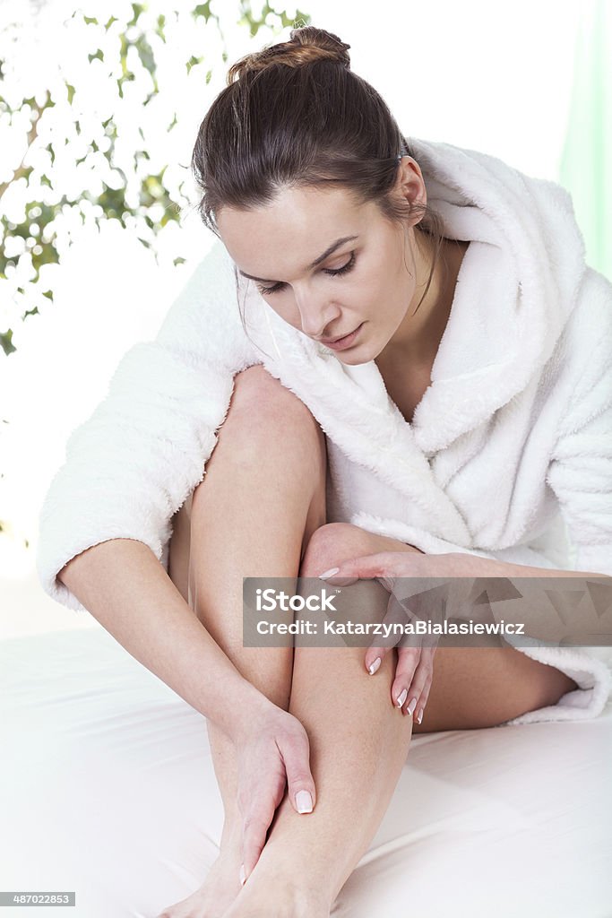 Woman rubbing her leg Young pretty woman rubbing her leg at home Bathrobe Stock Photo