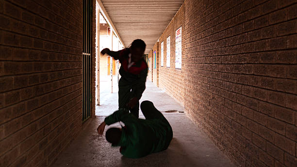 School kids fighting Two school kids fight in a dark passageway of their school, almost silhouette. bullying stock pictures, royalty-free photos & images