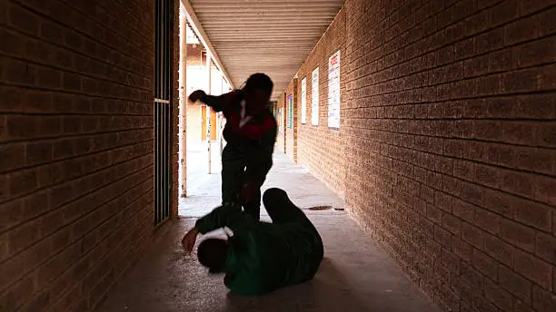 Two school kids fight in a dark passageway of their school, almost silhouette.