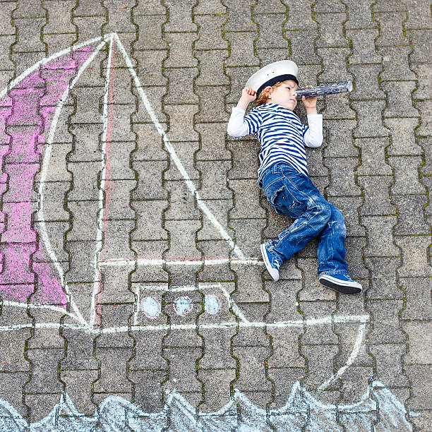 istock Little boy having fun with ship picture drawing with chalk 487039428