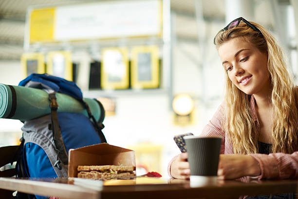 Catching up with the world A female traveller smiles as she catches up with loved ones on her travels. She is sat in a cafe in the terminal building on her mobile phone cafe sandwich stock pictures, royalty-free photos & images