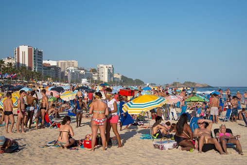 Rio de Janeiro, Brazil - August 29, 2015: Group of young people in swimwear standing and talking between the sunbathers on Ipanema beach in Rio the Janeiro.