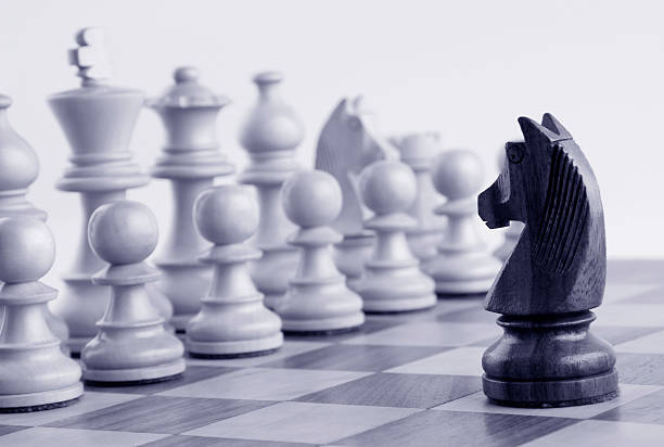 Black knight facing white chess pieces on a chess board Black knight facing white chess pieces on a chess board knight chess piece photos stock pictures, royalty-free photos & images