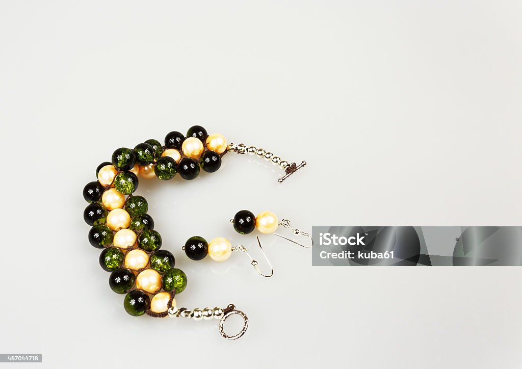 Handmade bracelet and two earrings isolated on a white backgroun Handmade bracelet and two earrings isolated on a white background.Jewelry made of three rows of beads green-black and pearly-yellow.Horizontal view. 2015 Stock Photo