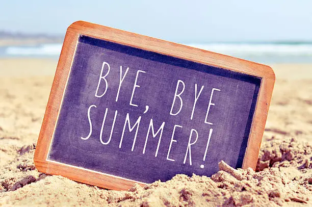 closeup of a chalkboard with the text bye, bye summer written in it, on the sand of a beach