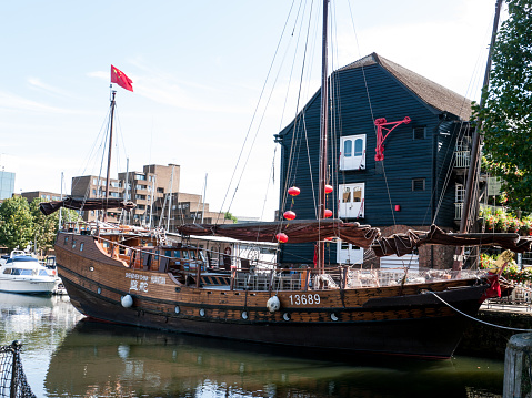 London, England - August 4, 2012: An old Chiness sailing ship with the national flag, moored in front of a brown warehouse building with a red hoist, in St. Katherine's Dock marina,  