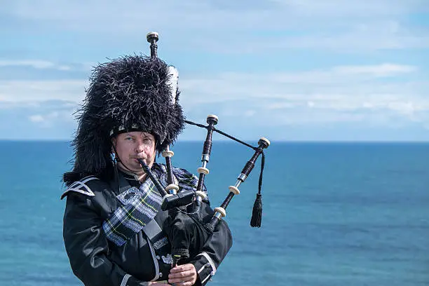 Traditional scottish bagpiper in full dress code at the sea