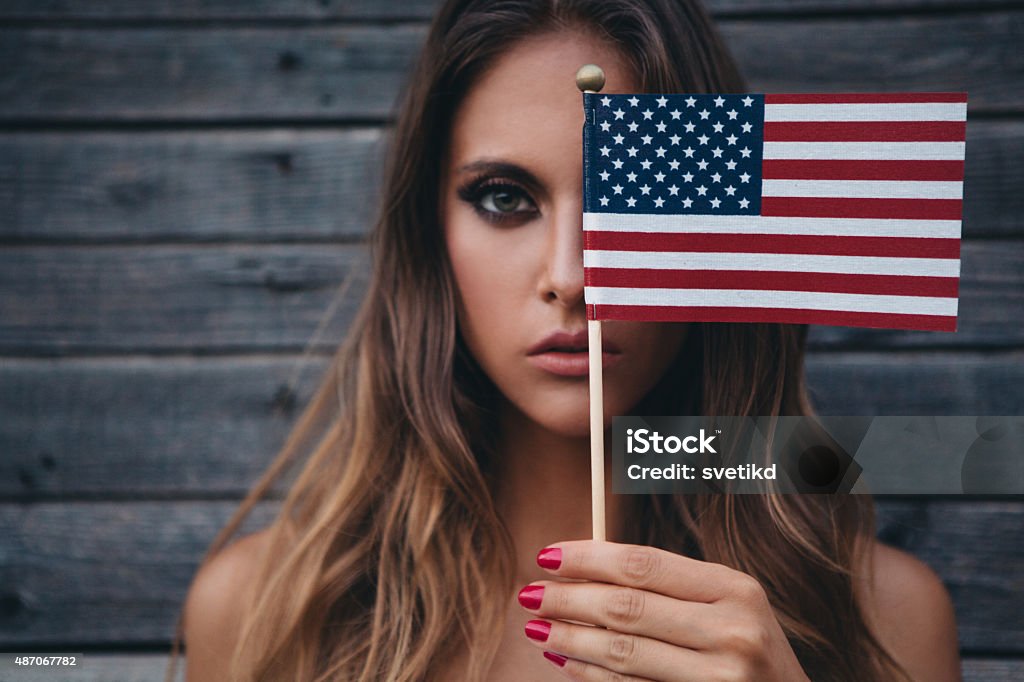 Young woman with American flag. Young woman holding American flag standing outside by wooden wall. Caucasian, long blond hair. Fourth of July Stock Photo