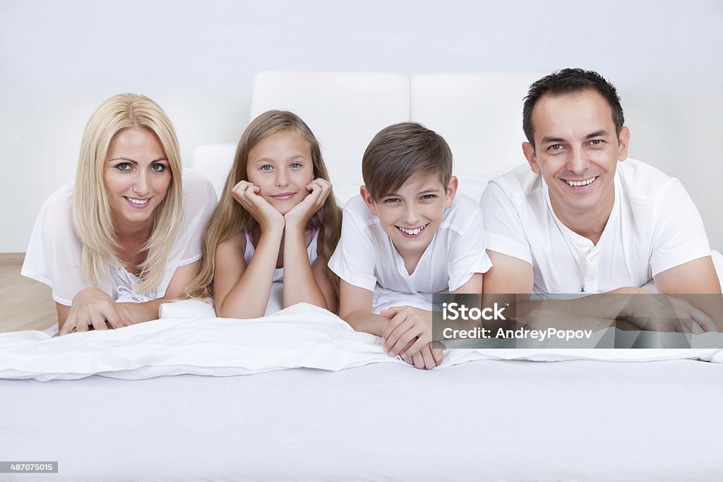 Happy Family With Two Children Lying On Bed Happy Family With Two Children Lying On Bed At Home 30-39 Years Stock Photo