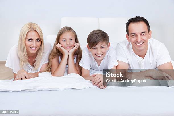 Happy Family With Two Children Lying On Bed Stock Photo - Download Image Now - 30-39 Years, Adult, Bed - Furniture