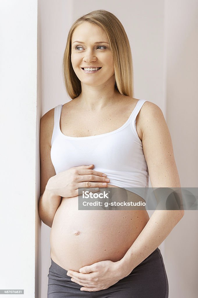 Waiting for a baby. Happy pregnant woman leaning at the wall and looking away Adult Stock Photo