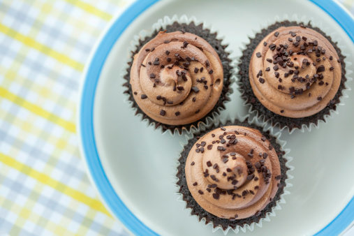 Three triple chocolate cupcakes on a plate with a patterned surface.