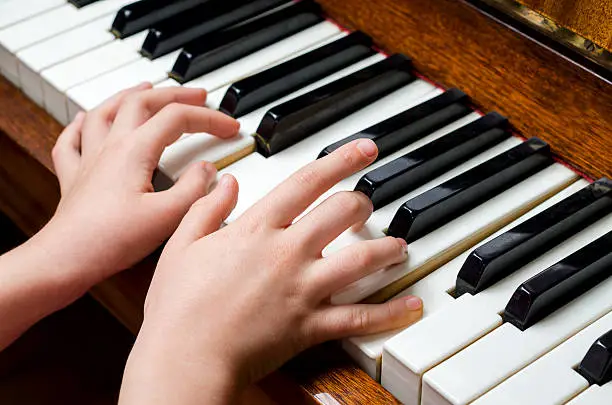 Llittle girl trying to play the piano with her little fingers.