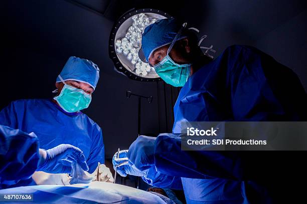 Surgeons Performing Complicated Surgery On Patient In Operating Room Stock Photo - Download Image Now