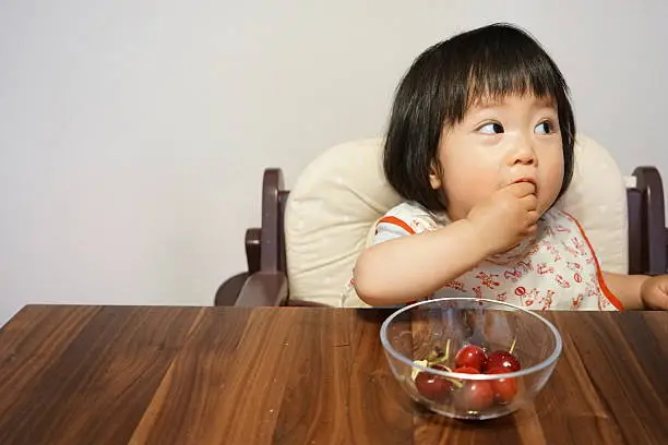 1-year old Japanese baby girl is eating fruits(cherry and banana)