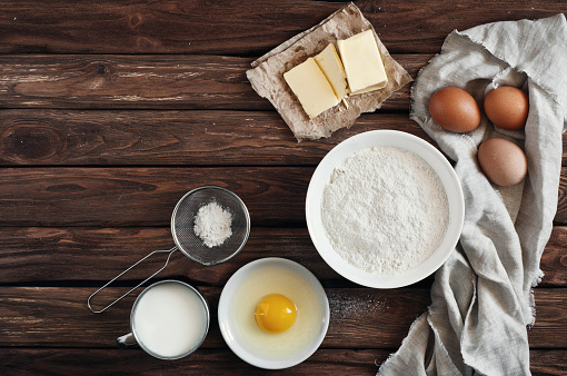ingredients for making pancakes or cake - flour, egg, butter, milk on  the old wooden background. top view. rustic or rural style. background with free text space.  Ingredients for the dough.