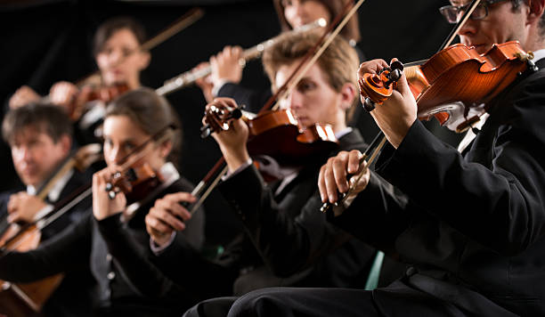Orchestra first violin section Symphony orchestra first violin section performing on dark background. orchestra photos stock pictures, royalty-free photos & images