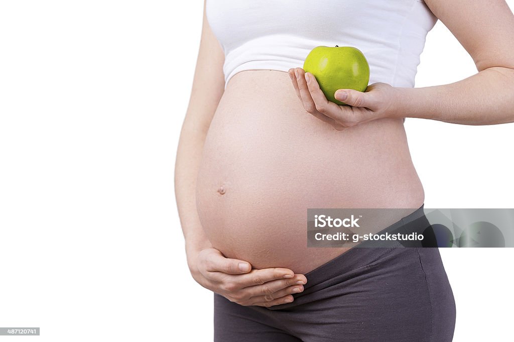 Only healthy food. Cropped image of pregnant woman holding green apple while standing isolated on white Adult Stock Photo