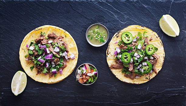 top down photo of two authentic mexican tacos top down photo of two authentic mexican street tacos on slate surface with onions, pico de gallo, salsa verde, limes, cilantro, and jalapeno peppers mexican food photos stock pictures, royalty-free photos & images