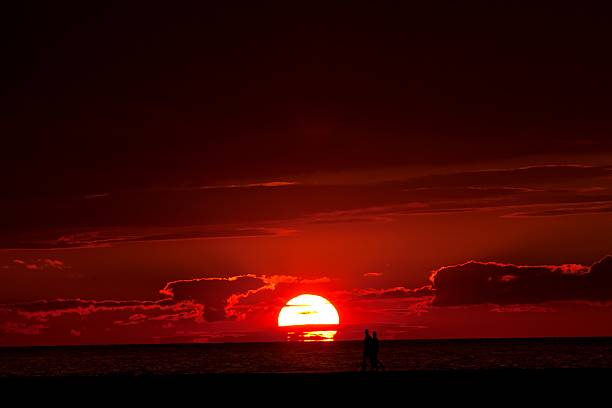 As the sun sets over Lake Michigan, a couple walk the North Breakwater Pier in Ludington Michigan. They are shown in silhouette.