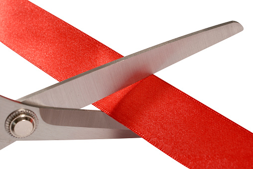 Close-up of scissors cutting red ribbon or tape against a white background