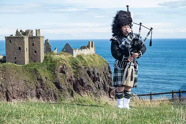 Traditional scottish bagpiper in full dress code at Dunnottar Castle