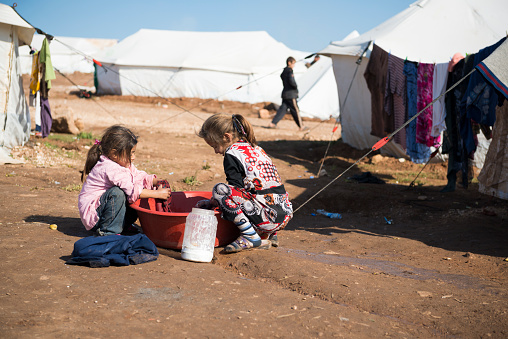 Atmeh, Syria - January 14, 2013: Two Syrian girls wash clothes outside their tent in the displaced persons camp in Atmeh, Syria. A boy walks by in the background.