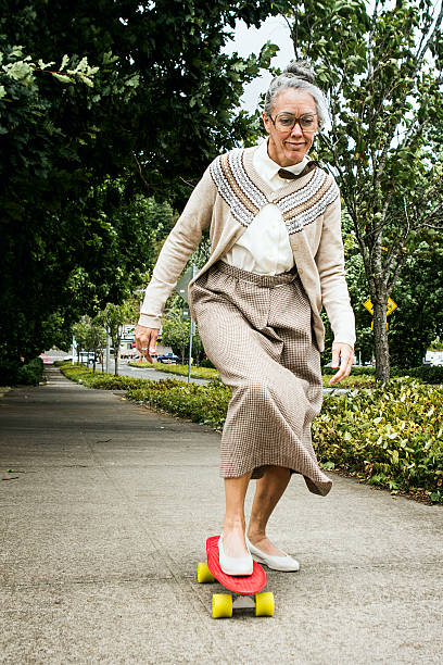A senior elderly woman attempting skateboarding pushed down the sidewalk with a smile on her face.   A great additional exercise and balance for her healthy lifestyle.  Vertical image.