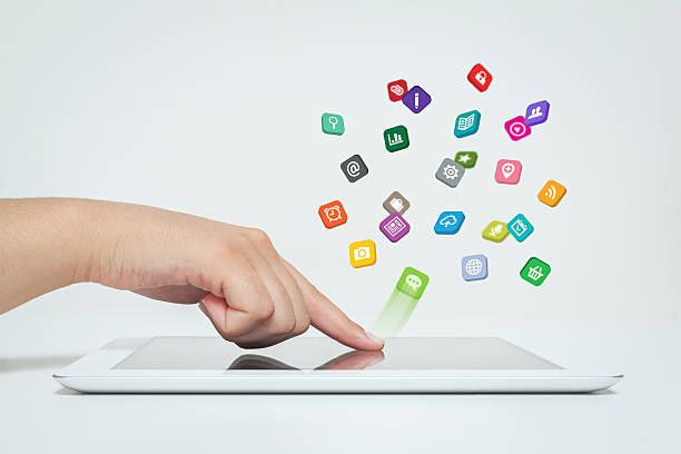 Female hand touching tablet computer icon. Woman touching screen and icons fly off tablet computer. Colorful computer icons make a group above tablet computer. Copy space on top left. Apps Store stock pictures, royalty-free photos & images