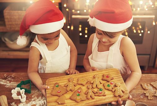 Christmas and New Year food preparation. Xmas gingerbread cooking and decorating freshly baked cookies with icing and mastic. Mom helping cute little daughter to decorate cookie on wooden messy table