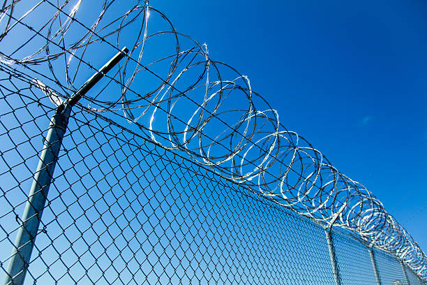 istock Razor Wire Coiled on Chainlink Fence with Deep Blue Sky 487160441