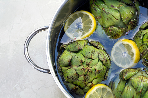 cooking artichokes, fresh artichokes with lemon slices and water in a stainless steel pot, Copy Space