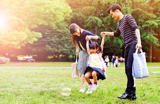 Family having a walk outdoors in summer in park, Tokyo, Japan. Parents are throwing their little daughter in the air in a playful way. Image is taken during Tokyo Istockalypse 2015