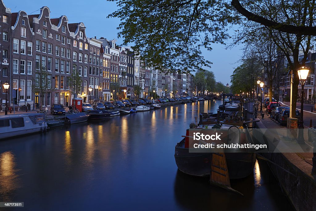 Amsterdam - Canal in the evening The picture shows a canal in Amsterdam in the evening with some old houses and the brunches of a tree. The lights of some lanterns reflected in the water. Amsterdam Stock Photo