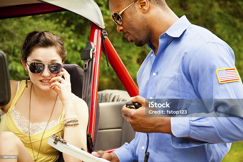 Policeman gives woman driver a traffic ticket for speeding. Young woman is pulled over by an African descent policeman for speeding. He is giving her a traffic ticket.  She is driving a sporty red Jeep. 20-29 Years Stock Photo