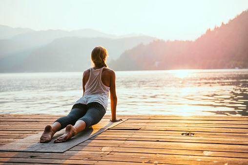 Beautiful woman practicing Yoga by the lake - Sun salutation series - Upward facing dog - Toned image