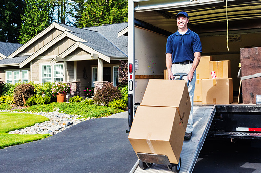 Photo of a delivery man unloading (or loading) truck, walking cardboard boxes down ramp on a hand truck.