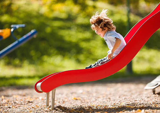 alegre niño pequeño divirtiéndose mientras corrediza al aire libre. - área de juego fotografías e imágenes de stock