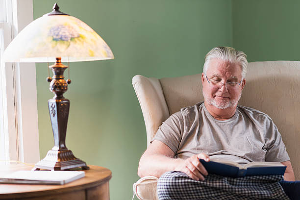 istock Senior man in living room reading book 487181064