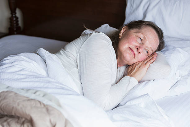 istock Senior woman lying in bed, eyes open, smiling 487181086