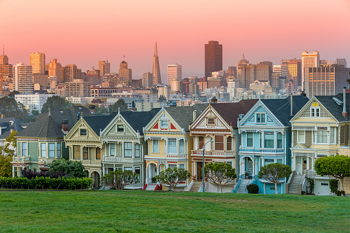 Classic shot of Victorian houses across the street from Alamo Square in San Francisco. Skyline of San Francisco is seen in background.
