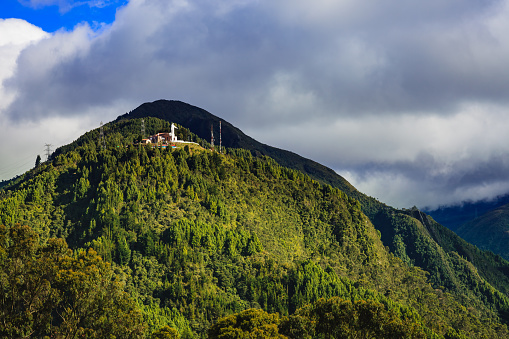 The peak of Guadalupe as seen from Monserrate in Bogotá, the capital city of Colombia in South America.  A statue of Mary, linked to the chapel dedicated to 'Our Lady of Guadalupe', can been seen on top of the peak. In the back ground, the Andes mountains and another peak can also be seen. Photo shot in the afternoon sunlight; horizontal format. No people.  Copy space.