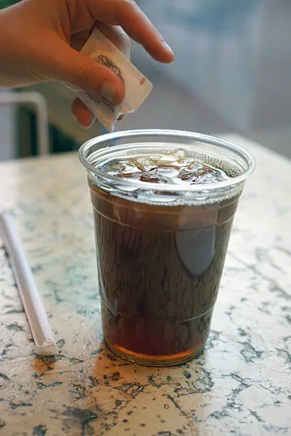 Hand pouring sugar sweetener into a plastic cup of iced-tea.
