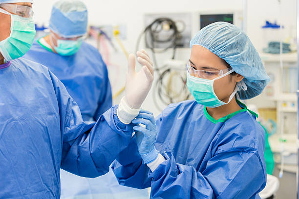 enfermera ayudando a cirugía o pasante cirujano poner en guantes estériles - hair net nurse scrubs asian ethnicity fotografías e imágenes de stock