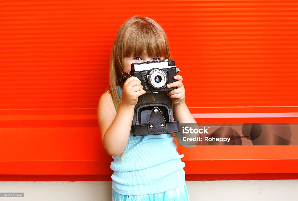 Little smiling girl child with old retro vintage camera against Little smiling girl child with old retro vintage camera against the colorful red wall 2015 Stock Photo