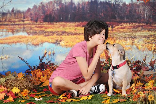 An attractive Hispanic girl  posing with her mutt as the dog accepts her reward - outside on a warm autumn day.