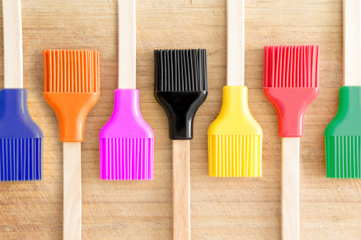 Colorful line of kitchen brushes in the colours of the rainbow for decorating and glazing pastries or basting meat arranged in an alternating pattern on a wooden background