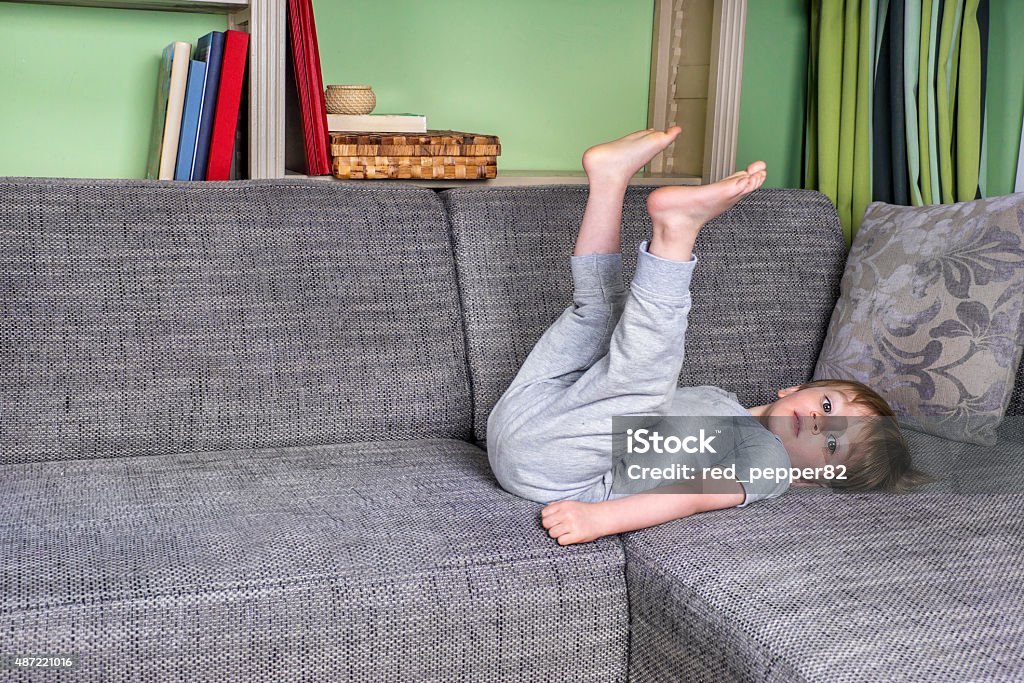 Little kid hanging around on the couch Little bored boy laying on the couch Boredom Stock Photo